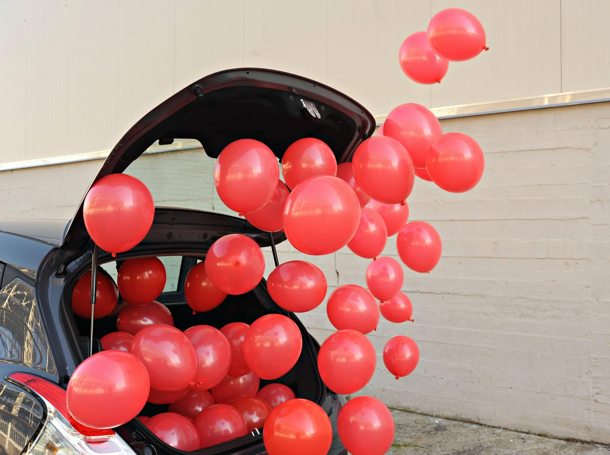 Rote Ballons steigen aus einem offenen Kofferraum