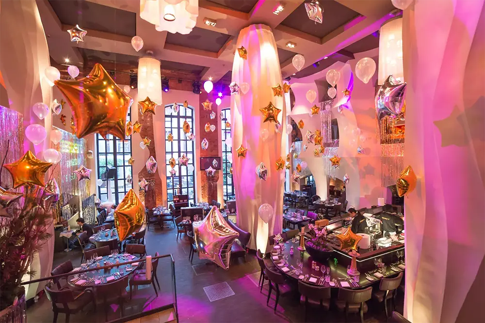 Veranstaltungsraum mit goldenen und silbernen Sternballons, weißen Ballons und rosa Beleuchtung